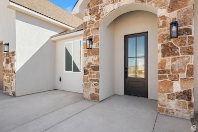 Entrance to property with stone siding, roof with shingles, and stucco siding