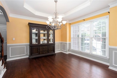 Unfurnished dining area featuring arched walkways, wainscoting, dark wood-style flooring, a chandelier, and a raised ceiling