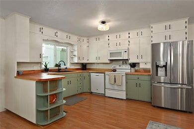 Kitchen featuring green cabinetry, open shelves, white appliances, light wood-type flooring, and a textured ceiling