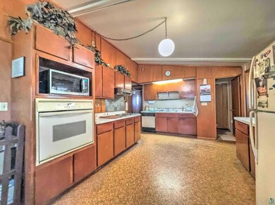 Kitchen featuring brown cabinets, under cabinet range hood, light floors, light countertops, and white appliances