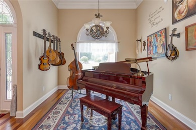 Sitting room with wood finished floors, a chandelier, ornamental molding, and baseboards