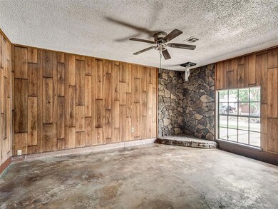 Unfurnished room with a stone fireplace, a textured ceiling, ceiling fan, and wood walls