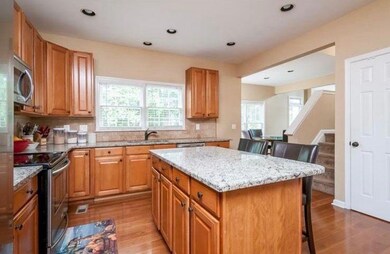 Kitchen with appliances with stainless steel finishes, light wood-style floors, tasteful backsplash, light stone countertops, and a breakfast bar area