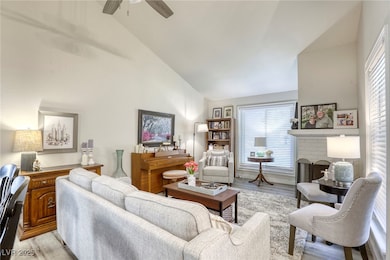Living area featuring light wood-type flooring, a fireplace, plenty of natural light, high vaulted ceiling, and ceiling fan