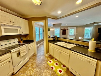 Kitchen with white appliances, a sink, dark countertops, crown molding, and recessed lighting
