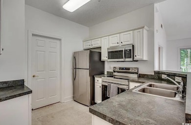 Kitchen featuring dark countertops, stainless steel appliances, white cabinetry, and a textured ceiling