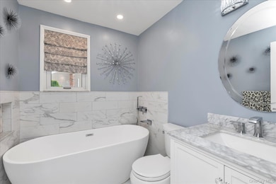 Bathroom with vanity, a soaking tub, tile walls, and recessed lighting