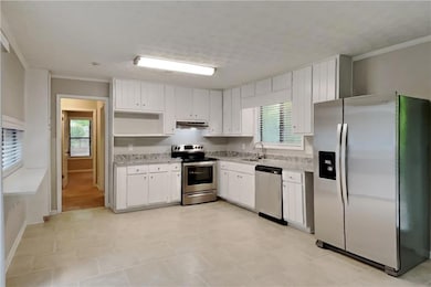 Kitchen with stainless steel appliances, healthy amount of natural light, under cabinet range hood, white cabinetry, and crown molding