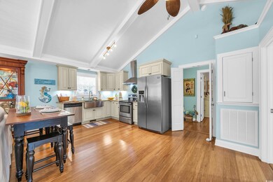 Kitchen with cream cabinets, beamed ceiling, appliances with stainless steel finishes, light wood-style flooring, and wall chimney exhaust hood