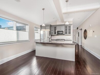 Kitchen with gray cabinetry, tasteful backsplash, glass insert cabinets, dark wood-type flooring, and a kitchen island with sink