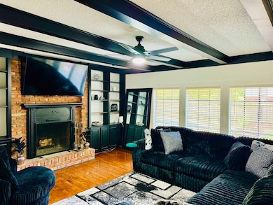 Living room featuring beam ceiling, wood finished floors, a textured ceiling, a brick fireplace, and a ceiling fan