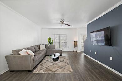 Spacious living room with dark wood flooring and spacious enough to accomendate a large sectional sofa or multiple sitting areas.  It has a ceiling fan, and natural light from a window and glass door, offering a cozy yet contemporary feel.