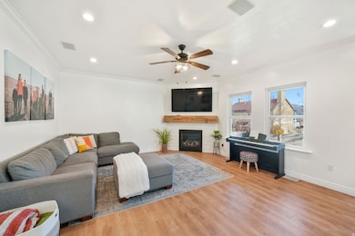 Living area featuring ornamental molding, a large fireplace, light wood-style flooring, ceiling fan, and recessed lighting