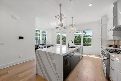 Kitchen featuring high end stove, a sink, a center island with sink, light wood-style flooring, and white cabinetry