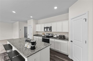 Kitchen featuring stone counters, a center island with sink, white cabinets, and appliances with stainless steel finishes