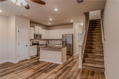 Kitchen featuring appliances with stainless steel finishes, white cabinetry, tasteful backsplash, a kitchen island with sink, and dark stone countertops