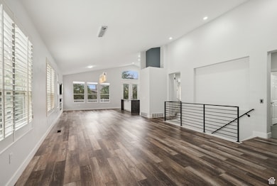 Unfurnished living room with high vaulted ceiling, dark wood-type flooring, and recessed lighting