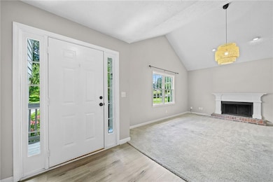 Entryway featuring wood finished floors, vaulted ceiling, a brick fireplace, and baseboards