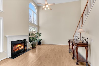 Unfurnished room with a high ceiling, a ceiling fan, wood finished floors, a fireplace, and stairs