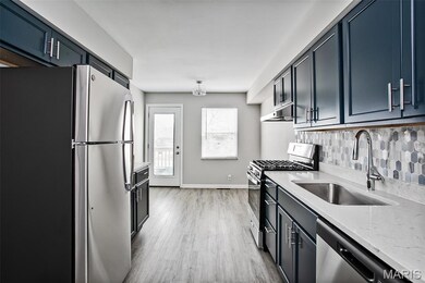 Kitchen featuring stainless steel appliances, a sink, light wood-style flooring, tasteful backsplash, and light stone countertops