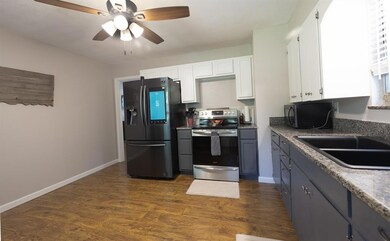 Kitchen with refrigerator with ice dispenser, stainless steel electric range oven, white cabinetry, dark wood-style flooring, and a ceiling fan