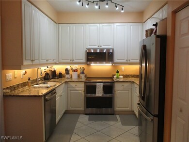 Kitchen with appliances with stainless steel finishes, sink, light tile patterned floors, dark stone counters, and white cabinets