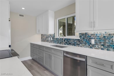 Kitchen featuring dishwasher, white cabinets, gray cabinetry, decorative backsplash, and light stone counters