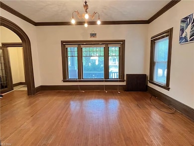 Empty room featuring ornamental molding, hardwood floors, radiator heating unit, and a chandelier