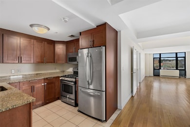 Kitchen featuring stainless steel appliances, light stone counters, brown cabinets, and light wood-style flooring