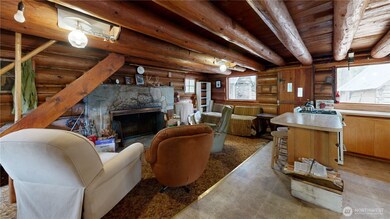 Inviting family room with log beam ceilings, stone fireplace, and open layout connecting to the kitchen.