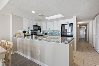 Kitchen with a peninsula, black appliances, dark stone counters, backsplash, and white cabinets