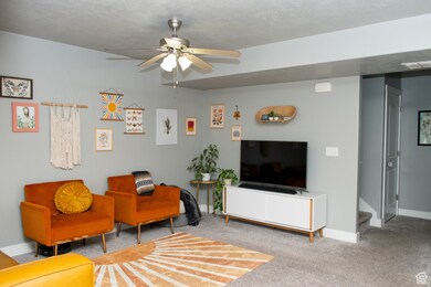 Carpeted living area featuring ceiling fan and baseboards