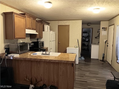 Kitchen with a peninsula, brown cabinetry, a textured ceiling, under cabinet range hood, and light countertops