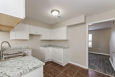 Kitchen with white cabinetry, dark tile patterned flooring, and light stone countertops