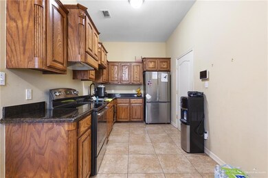 Kitchen with black range with electric cooktop, freestanding refrigerator, brown cabinets, light tile patterned floors, and dark stone counters