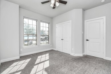 This is a bright, modern guest bedroom/study with tall ceilings and large windows that provide ample natural light. It features plush carpeting, fresh neutral paint, and a ceiling fan. There are two white doors, one likely a closet and the other an entrance.