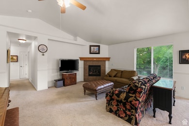 Living area with light carpet, lofted ceiling, a tiled fireplace, and ceiling fan