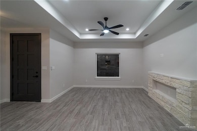 Unfurnished living room with wood finished floors, a tray ceiling, a stone fireplace, ceiling fan, and recessed lighting