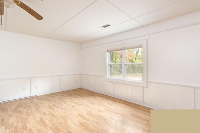 Empty room with light wood-style flooring, a wainscoted wall, and a ceiling fan