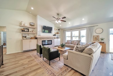 Living area featuring vaulted ceiling, light wood-style floors, ceiling fan, a fireplace, and recessed lighting