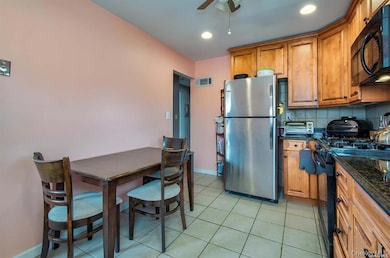 Kitchen featuring brown cabinets, decorative backsplash, black appliances, dark stone counters, and light tile patterned floors