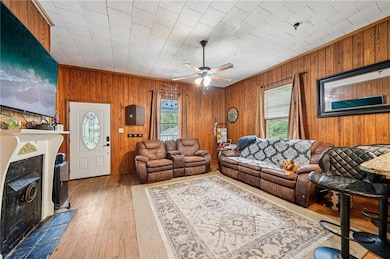 Living area featuring light wood finished floors, wooden walls, ceiling fan, and a fireplace with flush hearth