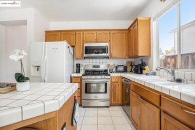 Kitchen with stainless steel appliances, tile countertops, light tile patterned floors, and brown cabinets