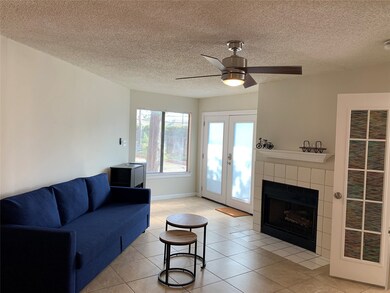 Living area featuring a textured ceiling, a ceiling fan, light tile patterned floors, a fireplace, and french doors