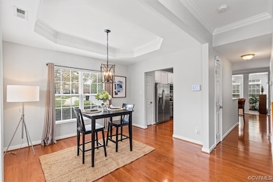 Hardwood floored dining room featuring crown molding, a tray ceiling, and a chandelier