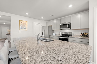 Kitchen with appliances with stainless steel finishes, a breakfast bar, light stone countertops, recessed lighting, and a kitchen island with sink