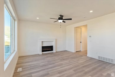 Unfurnished living room with recessed lighting, light wood-style flooring, a warm lit fireplace, and a ceiling fan