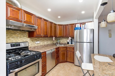 Kitchen featuring appliances with stainless steel finishes, under cabinet range hood, decorative backsplash, hanging light fixtures, and recessed lighting