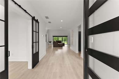 Corridor with a barn door, light wood-style flooring, and recessed lighting