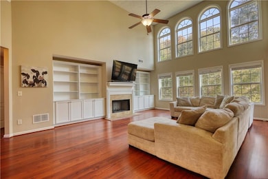Living room with a high ceiling, a high end fireplace, dark wood finished floors, ceiling fan, and built in features